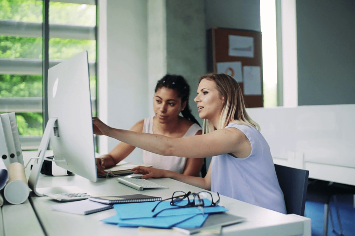 Two young women with computer sitting at the desk in the office working ZumaZip